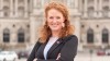 Fiona Fiedler, NEOS-Sprecherin für Menschen mit Behinderungen, lächelt und posiert für ein Foto mit einem Gebäude im Hintergrund. 
