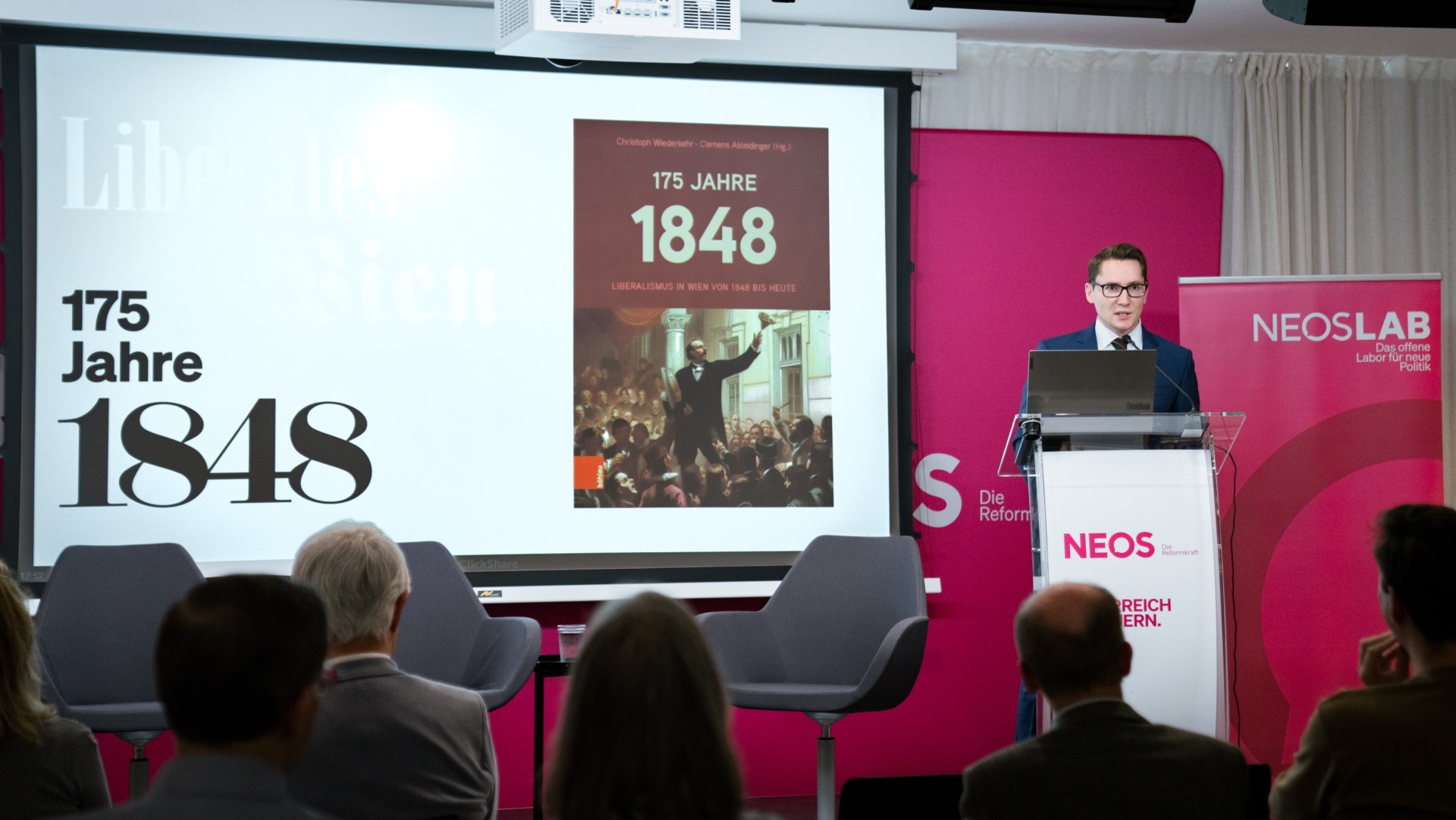 Clemens Ableidinger am Rednerpult vor einer Leinwand mit dem Buchcover "175 Jahre 1848"