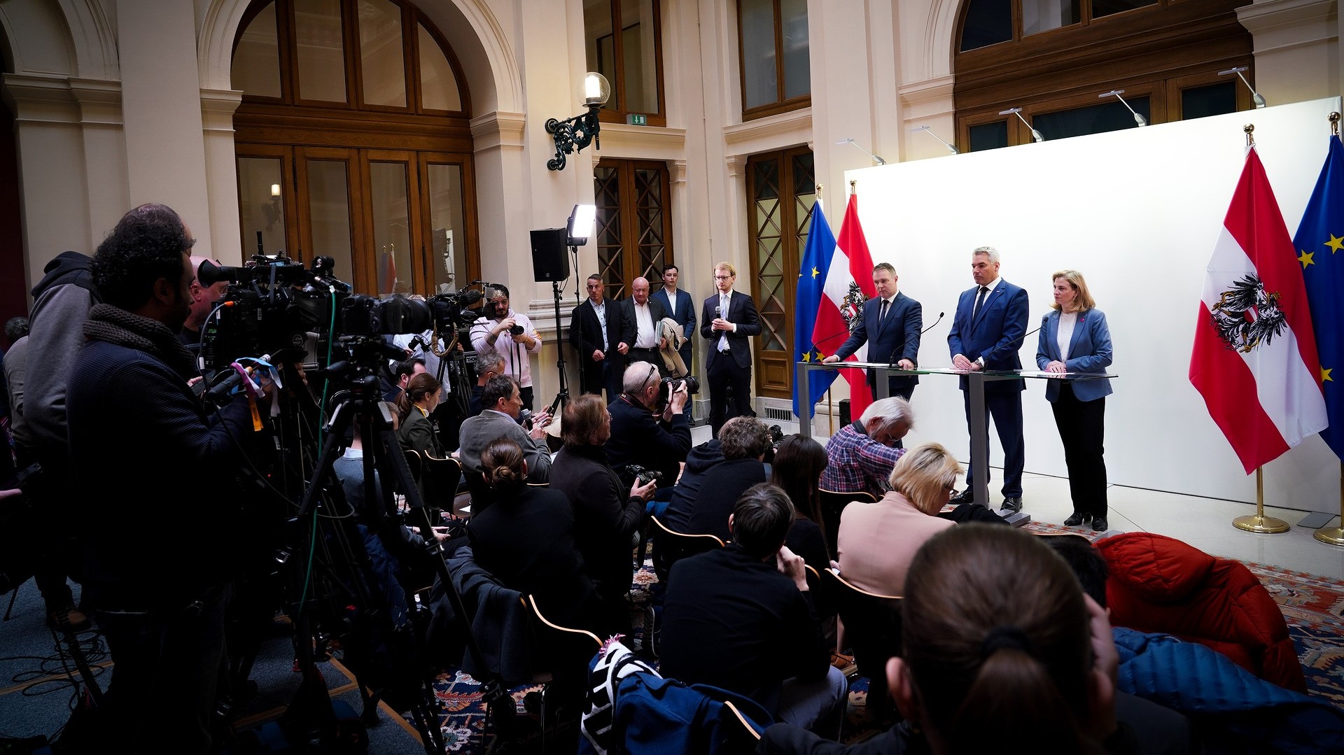 Beate Meinl-Reisinger (NEOS), Karl Nehammer (ÖVP) & Andreas babler (SPÖ) stehen auf einem Podium während der Pressekonferenz vom 18. Nov. 2024 vor den Medien und kündigen die Dreier Regierungskoalitionsverhandlungen an.