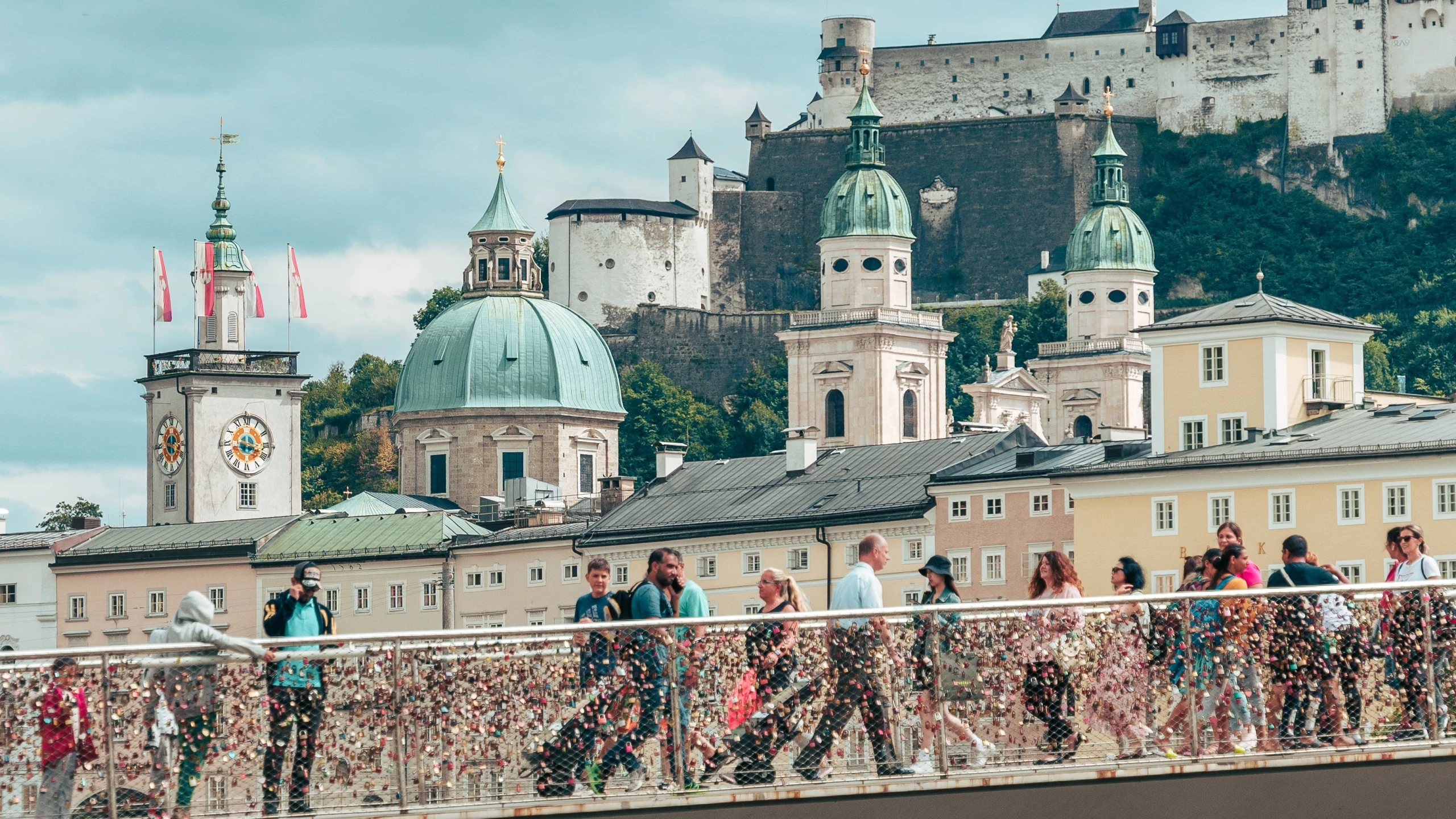 Salzburg: Menschen überqueren Makartsteg mit Blick auf Festung Hohensalzburg und Kirchtürme.