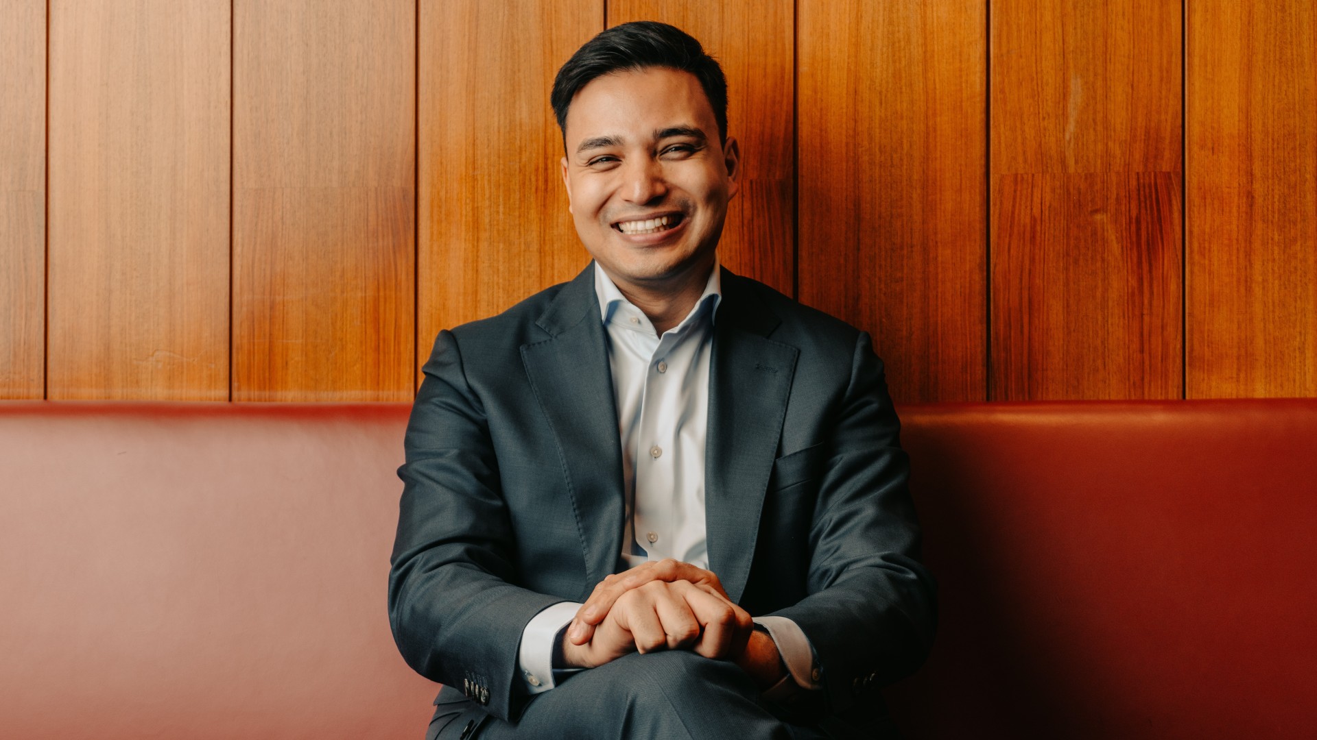 Yannick Shetty lächelt und sitzt auf einer banck