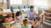 Kindergartenpädagoge sitzt mit spielenden Kindern an einem Tisch