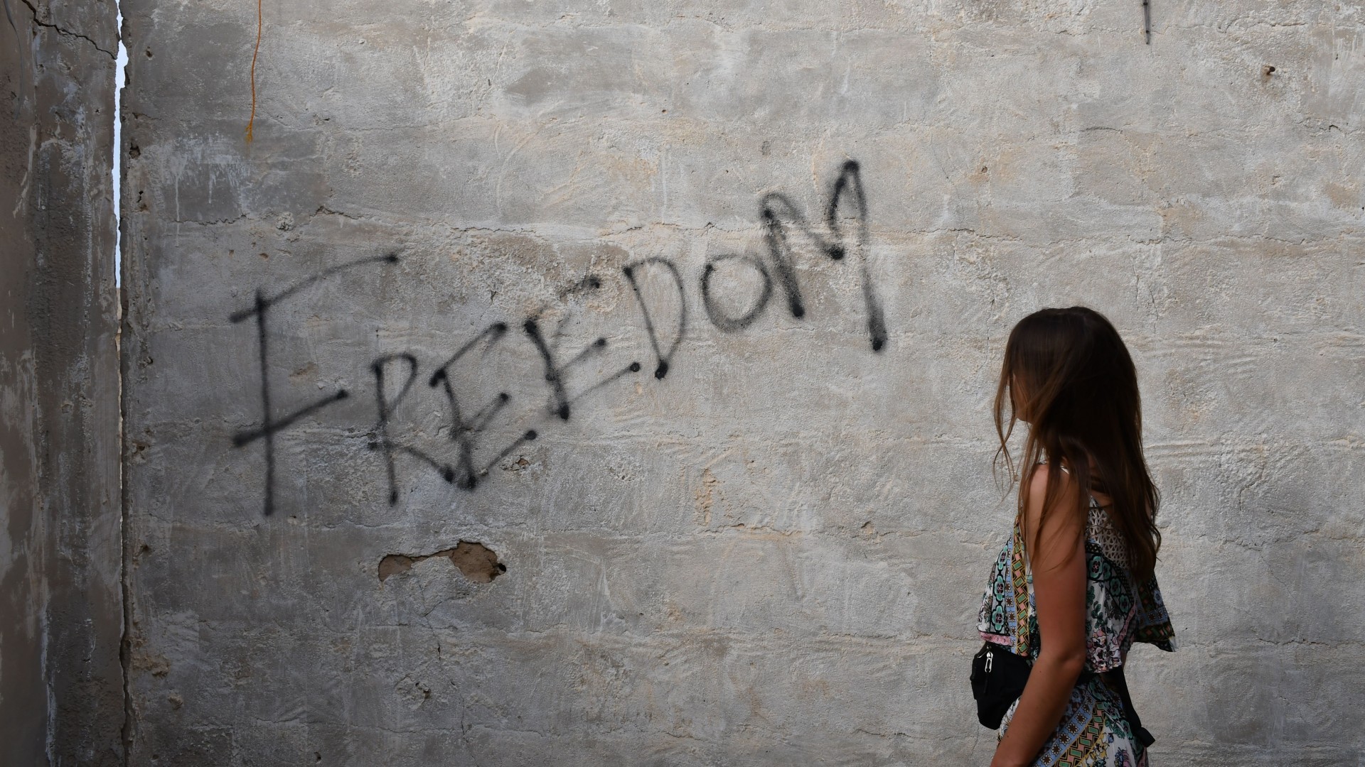 Eine Betonwand, auf die "Freedom" gesprüht ist. Ein Mädchen geht vorbei.