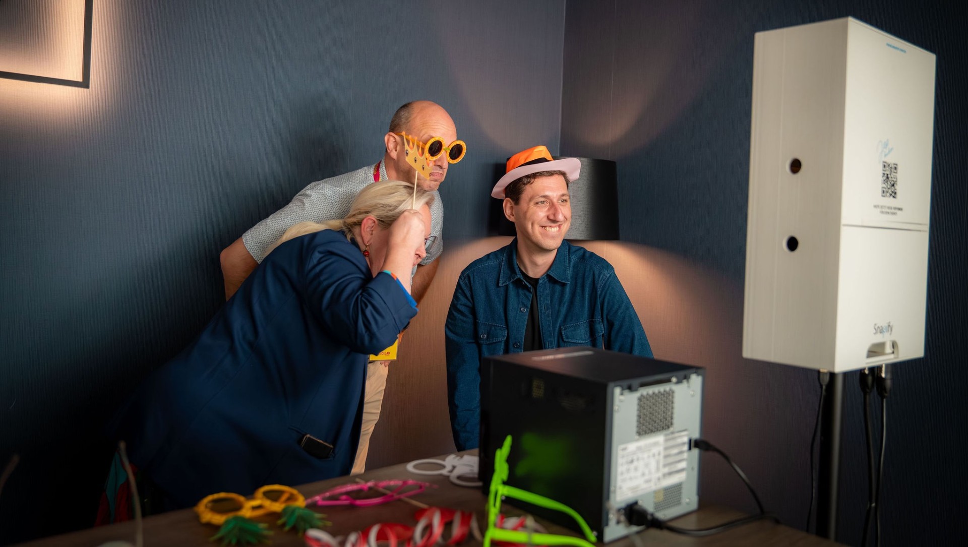 Drei Personen mit lustigen Hüten und Sonnenbrillen vor einer Fotobox