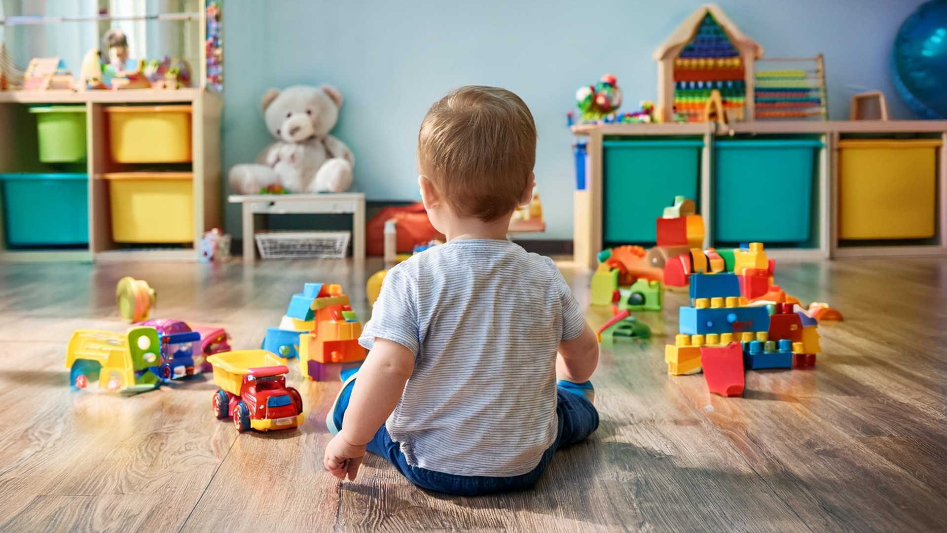 Firefly ein Kleinkind, das von hinten zu sehen ist, spielt mit buntem Kinderspielzeug auf dem Boden -2688x1513