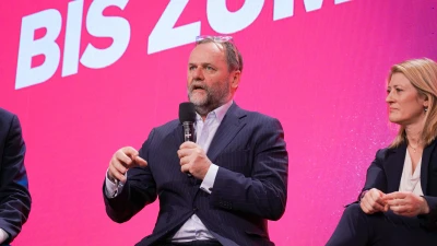 Michael Schickhofer spricht auf der Bühne vor pinkem Hintergrund mit Schriftzug.