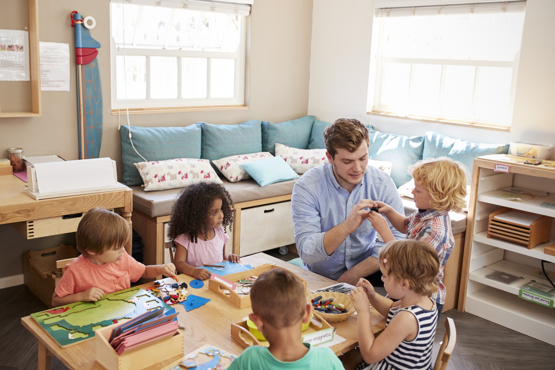 Kindergartenpädagoge und spielende Kinder sitzen um einen Tisch