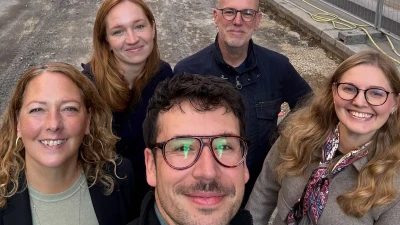 Fünf Personen lächeln in die Kamera, im Hintergrund Baustelle