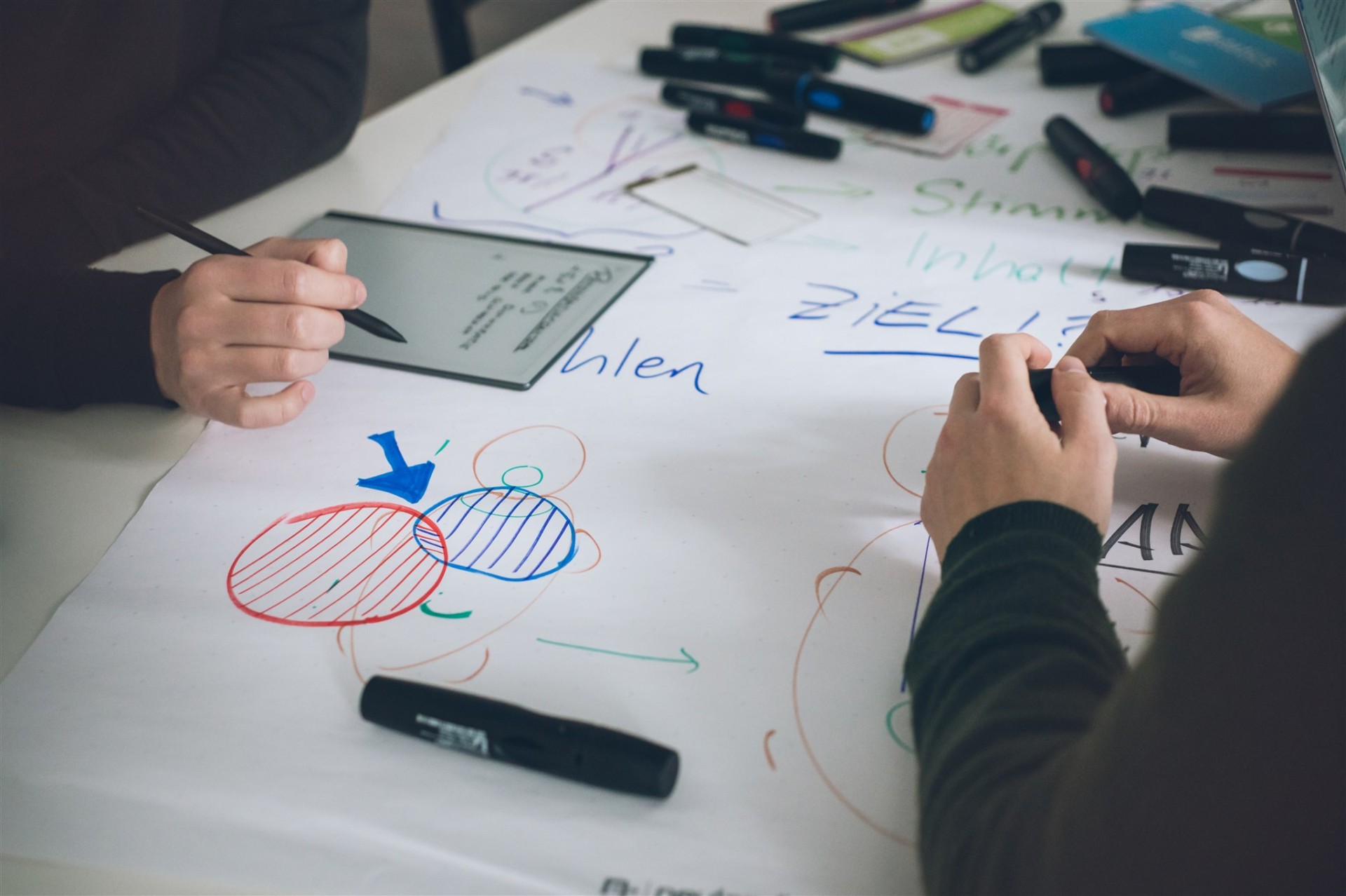 Eine Gruppe von Personen arbeitet zusammen an einer weißen Tafel, mit Stiften und einem Laptop.