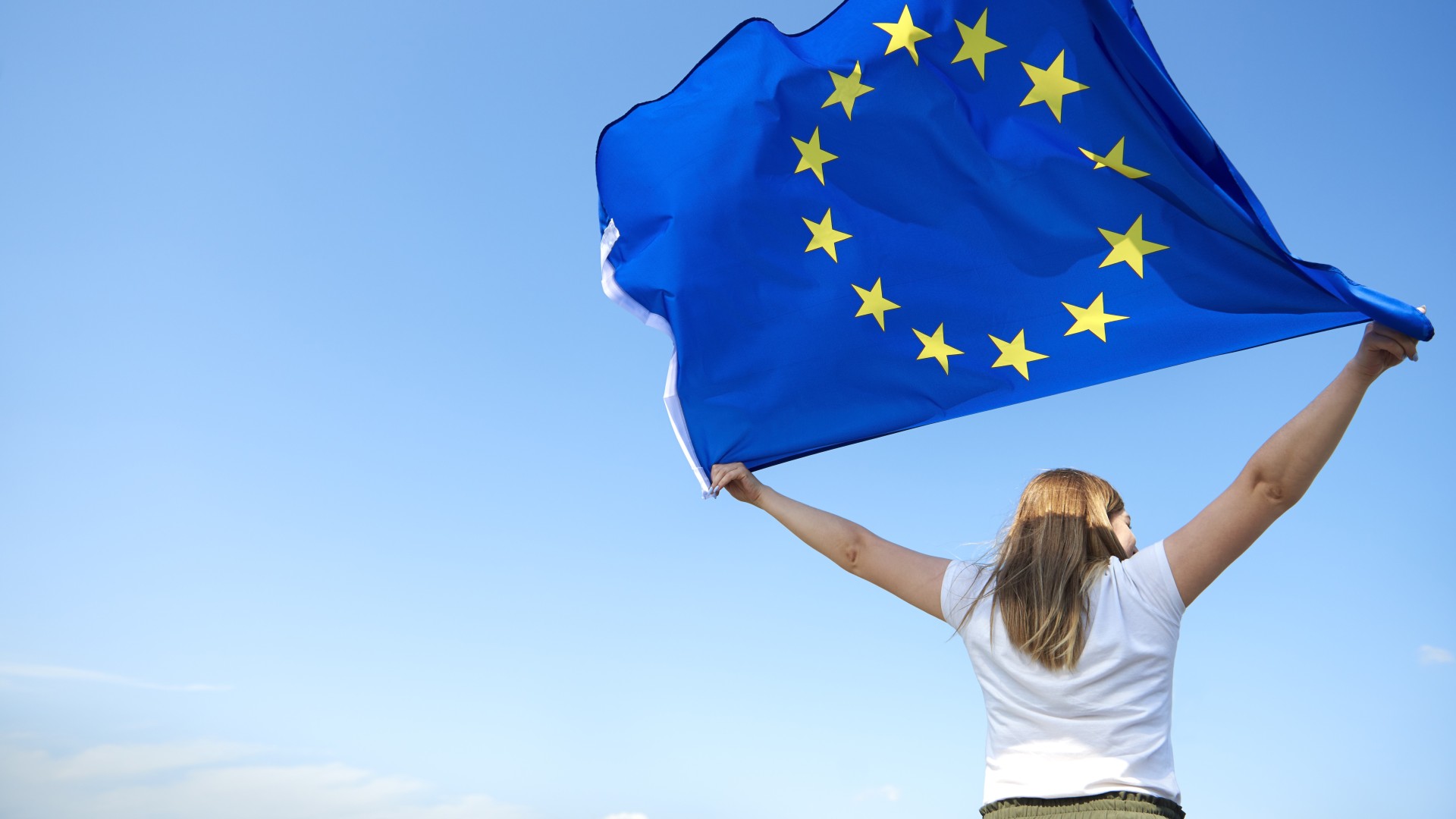 rueckansicht-der-jungen-frau-die-die-flagge-der-europaeischen-union-schwenkt.jpg
